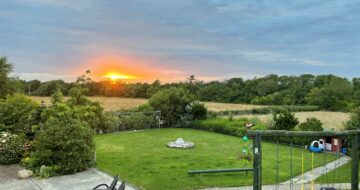 View from the balcony at Woodvilla Lodge - sunsetting beyond green fields and garden below